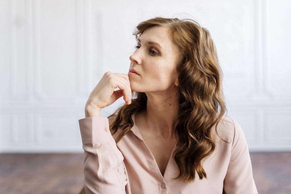 A thoughtful woman with curly hair sits indoors